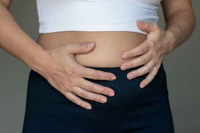Close-up of a woman holding her bloated stomach with both hands.