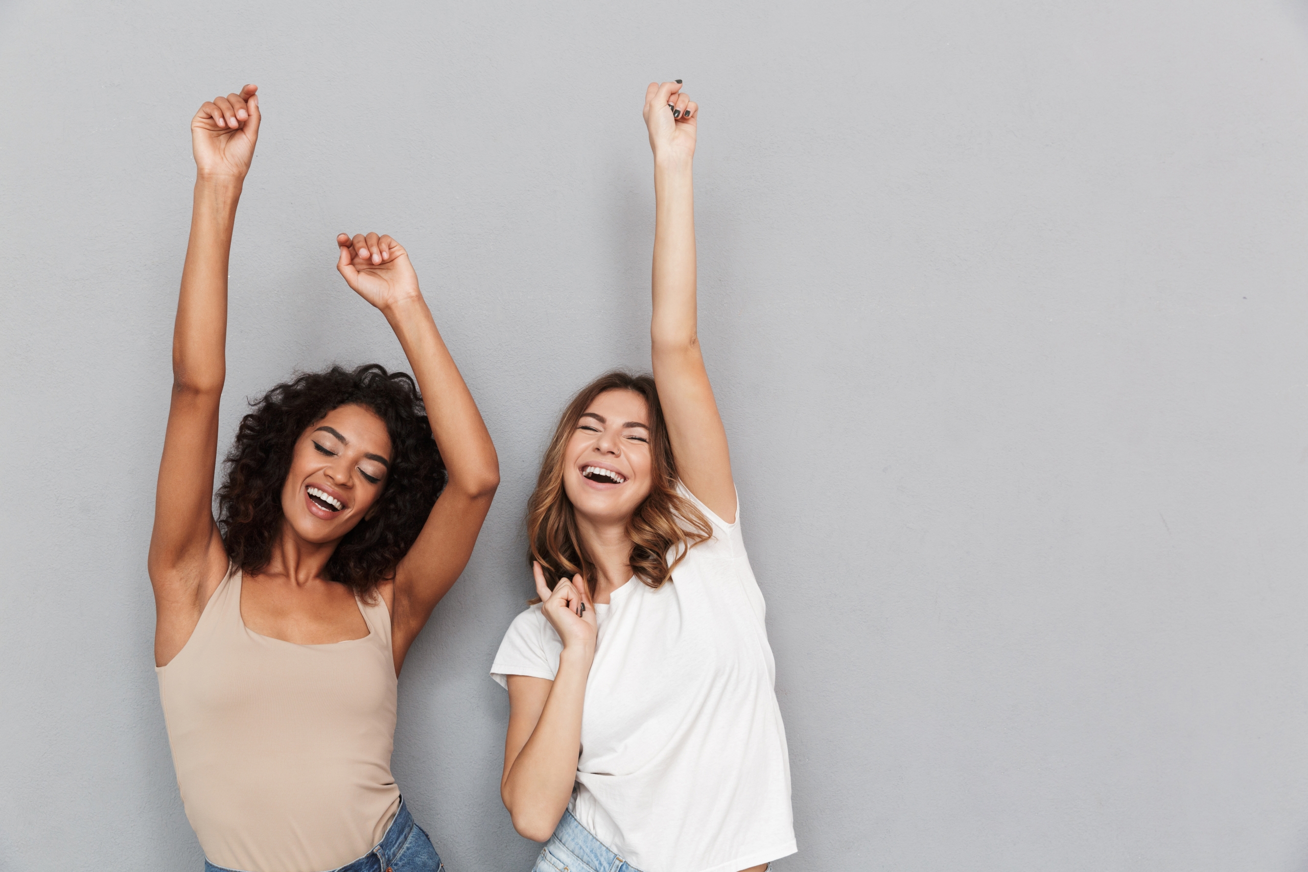 Portrait of two happy young women dancing and having fun isolated over gray background