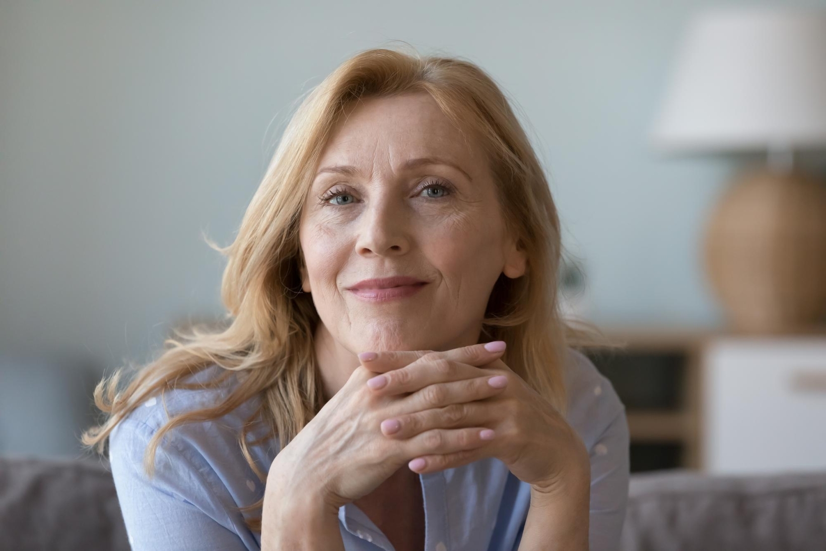 Portrait of a smiling mature blonde woman resting her chin on her clasped hands at home